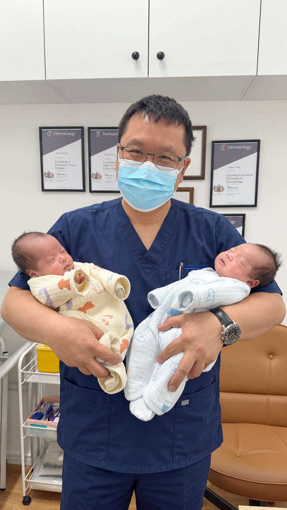 James in clinical scrubs holding two newborn babies